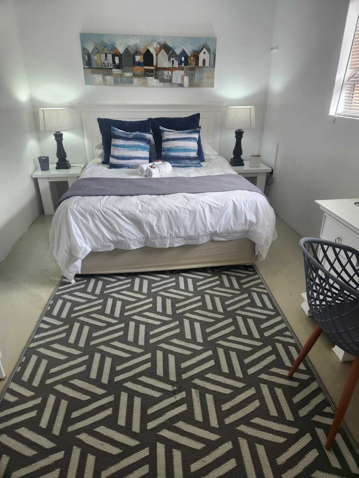 Um quarto bem arrumado com uma cama, mesas de cabeceira, uma cadeira, um tapete estampado e um quadro na parede.