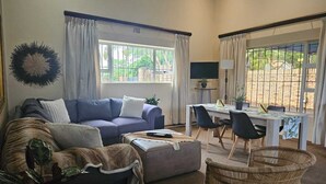 A living room with a sofa, ottoman, and a dining table with chairs. - Hillton Manor Guest House (Richards Bay)