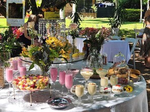A table set outdoors with various food items and drinks, surrounded by greenery and a garden. - Hillton Manor Guest House (Richards Bay)