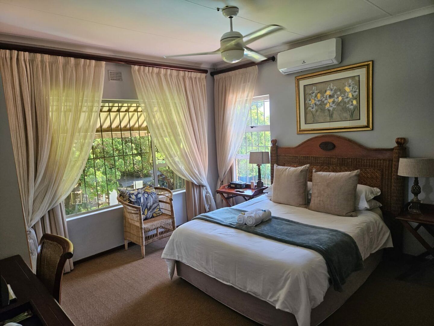 A hotel room with a bed, a desk, a chair, a ceiling fan, and an air conditioning unit.