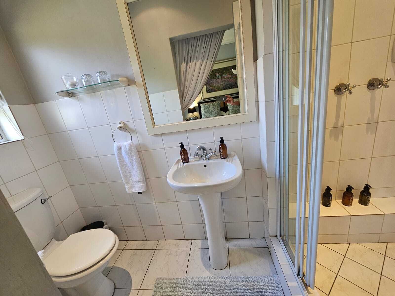 Un baño con lavamanos blanco, inodoro, cabina de ducha de vidrio y espejo sobre el lavamanos.