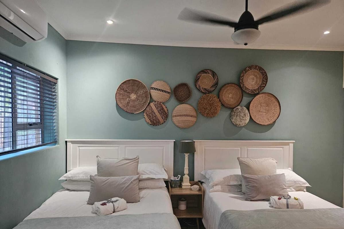 A hotel room with two beds, a ceiling fan, and a wall decorated with woven baskets.