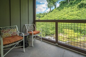 Un balcón con dos sillas blancas y una pequeña mesa, con vistas a un paisaje verde exuberante y un arroyo.