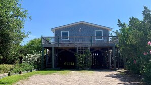 A two-story house with a balcony, surrounded by greenery and a gravel driveway. - Bluefin: Nautical and eclectic artwork, and amazing marsh views. (Ocracoke)