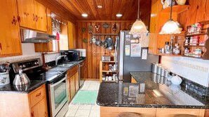 A kitchen with wooden cabinets, a central island, a sink, and a stove. - Bluefin: Nautical and eclectic artwork, and amazing marsh views. (Ocracoke)