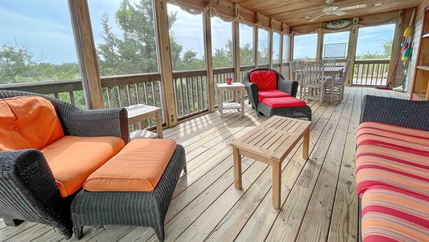 A covered outdoor deck with wicker furniture, a table, and a ceiling fan. - Bluefin: Nautical and eclectic artwork, and amazing marsh views. (Ocracoke)