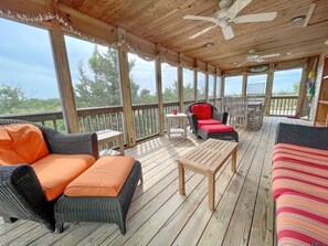A covered outdoor deck with wicker furniture, a table, and a ceiling fan. - Bluefin: Nautical and eclectic artwork, and amazing marsh views. (Ocracoke)