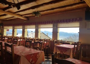 Ein Restaurant mit Holztischen und -stühlen, großen Fenstern mit Bergblick und einem Strohdach.