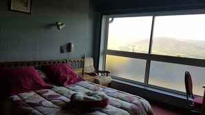 A bedroom with a large bed, a chair, a bedside table, a telephone, and a window with a view of mountains. - O'Friendly Gold Cottage 14 (Dorres)