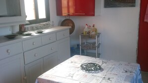 Una cocina con una mesa cubierta con manteles con motivos de París, un armario rojo y un cuadro de un molino.