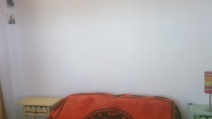 Un dormitorio con una cama cubierta por un edredón estampado, un ventilador de techo, una mesita y una estantería en la pared.