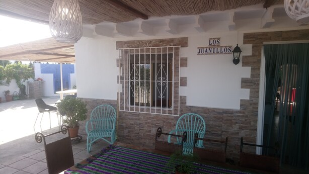 Un patio con dos sillas turquesa, una mesita y un letrero que dice "LOS JUANILLOS".