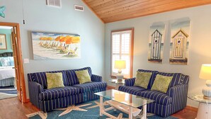 A living room with striped sofas, a glass coffee table, starfish-patterned rugs, and beach-themed wall art. - Cabana III:  Perfect getaway for two that offers a shared pool. (Ocracoke)