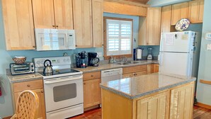 A kitchen with wooden cabinets, a microwave, a stove, a coffee maker, and a refrigerator. - Cabana III:  Perfect getaway for two that offers a shared pool. (Ocracoke)