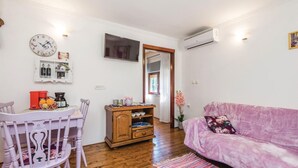 Una sala de estar acogedora con suelo de madera, un sofá rosa, una mesa de comedor blanca con sillas, un aparador de madera y un televisor montado en la pared.