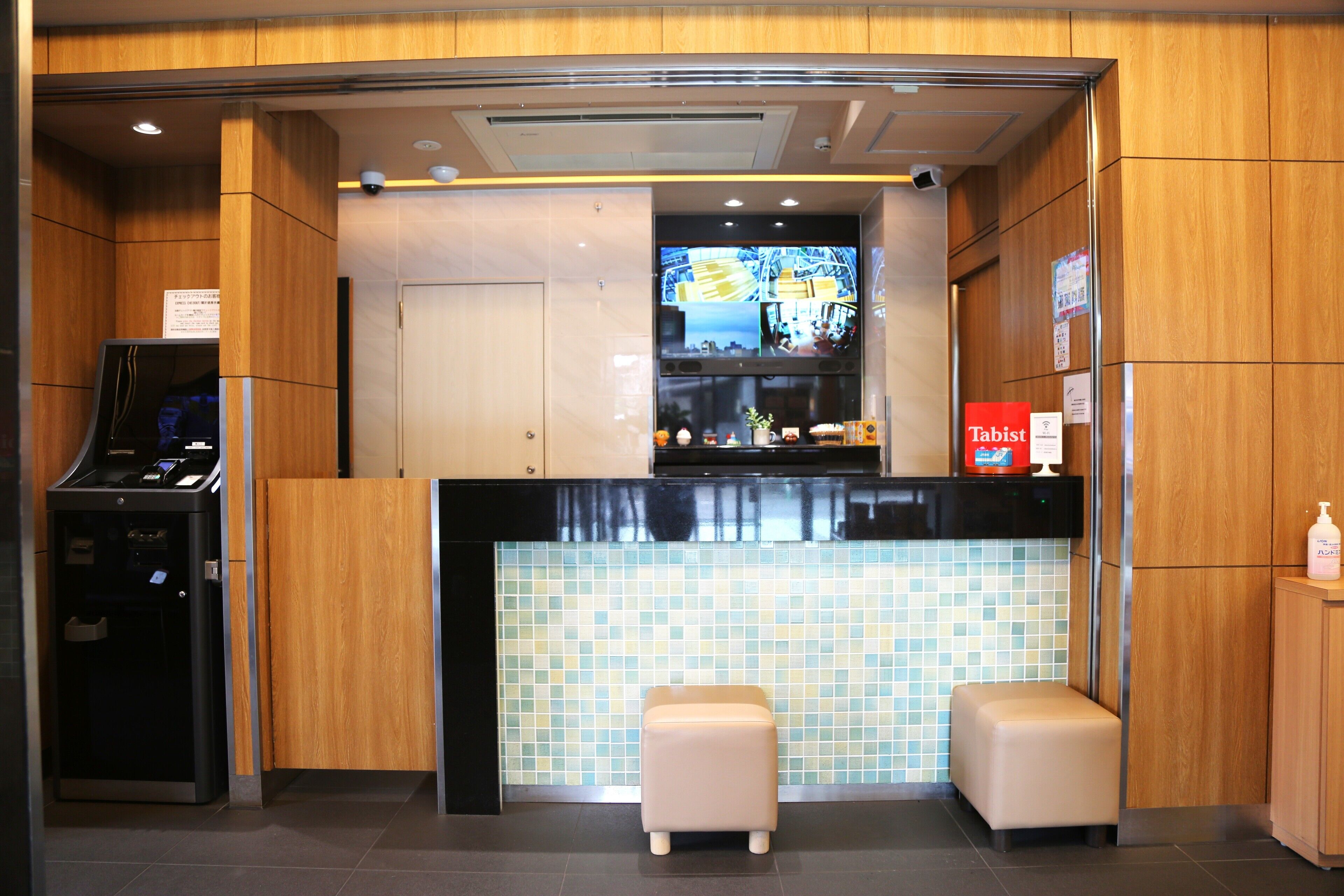 A reception area with a digital kiosk, a television screen, and two cushioned seating areas.