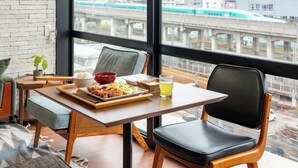 A dining area with a table set for a meal, a chair, and a view of a cityscape with a train. - TOKYO CITY VIEW HOTEL TABATA-STATION (Tokyo)