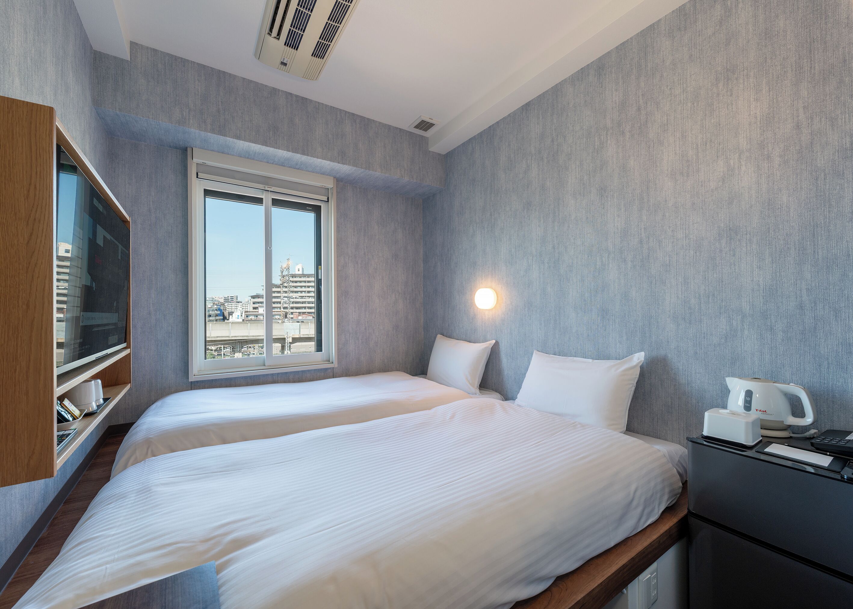 A hotel room with two beds, a TV, a kettle, and a view of the city.