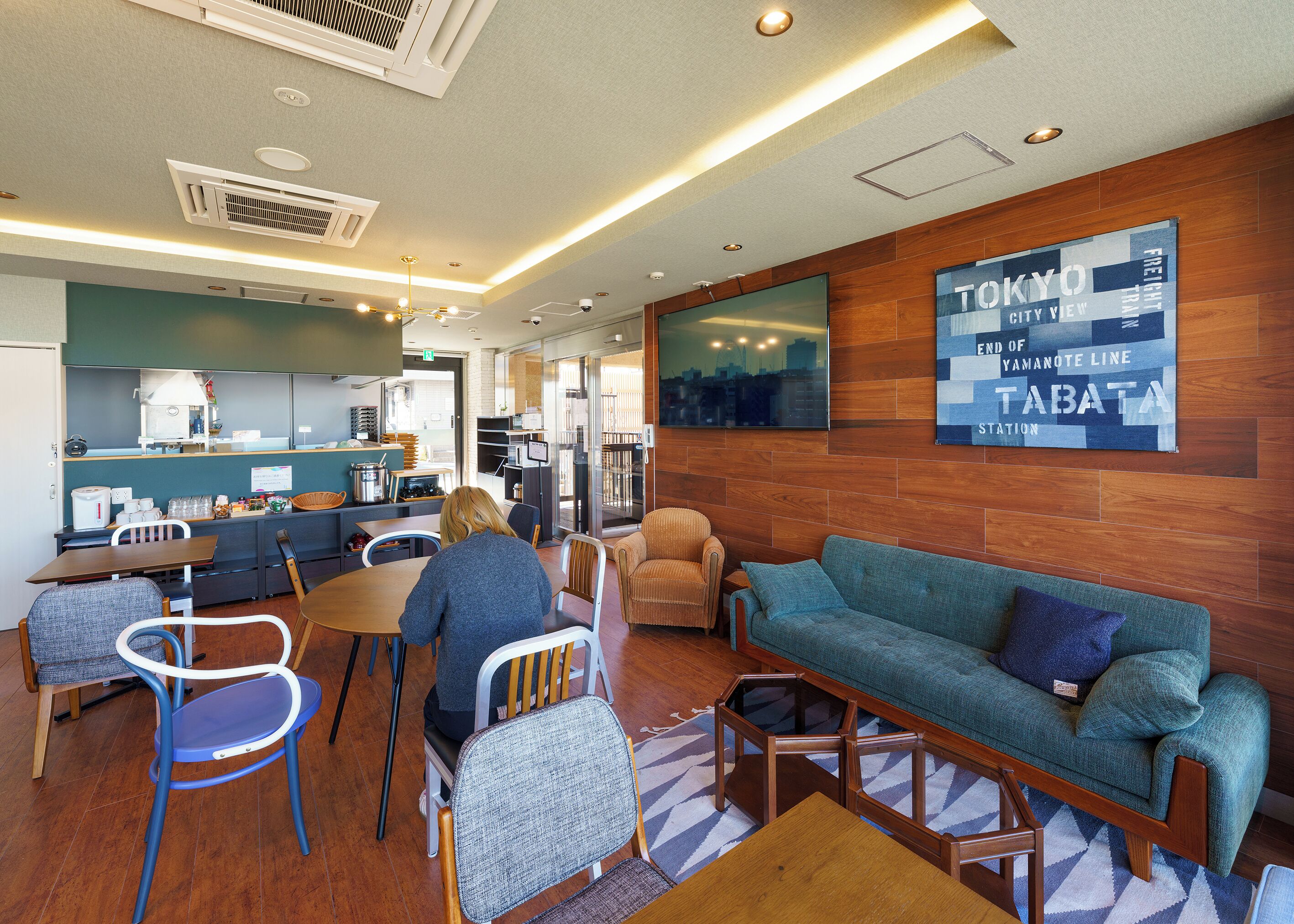 A modern lounge area with seating, a kitchen, and a city view wall.
