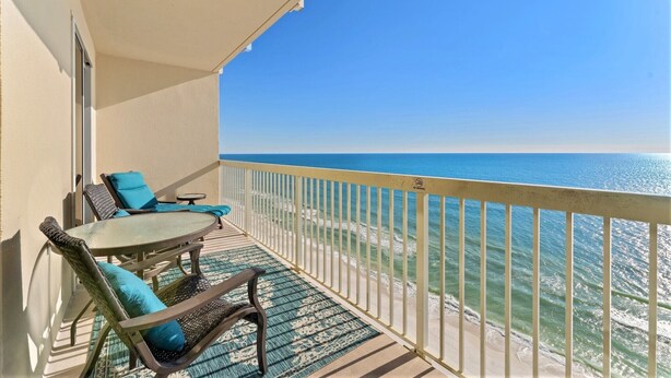 Ein Balkon mit Tisch und Stühlen mit Blick auf einen Strand und klares, blaues Wasser.