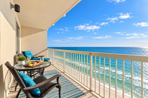 A balcony with a table set for dining, a chair, and a view of the ocean.