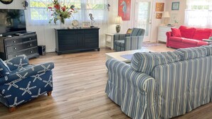 A living room with a wooden floor, a dark blue sofa with a star pattern, a striped sofa, a red couch, and a black entertainment unit with a TV. - Livin' Outta Line:  Canal front home with private dock, sunrise views. (Ocracoke)
