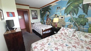A hotel room with two beds, a desk with a computer, a mural of a pirate scene, and a door.