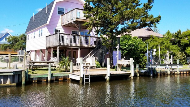 A pink house with a balcony and a dock extending into a body of water. - Livin' Outta Line:  Canal front home with private dock, sunrise views. (Ocracoke)