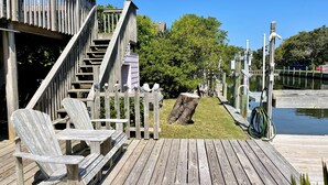 A wooden deck with Adirondack chairs and a staircase leading to a covered area. - Livin' Outta Line:  Canal front home with private dock, sunrise views. (Ocracoke)