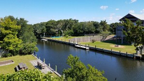 A riverside view with a dock, grassy areas, and a building with a balcony. - Livin' Outta Line:  Canal front home with private dock, sunrise views. (Ocracoke)