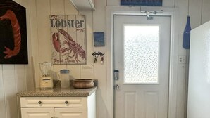 A kitchen with white cabinets, a blender, a pot, and a lobster poster on the wall. - Livin' Outta Line:  Canal front home with private dock, sunrise views. (Ocracoke)