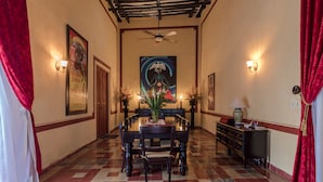 Un comedor con piso a cuadros, una mesa central con sillas, un ventilador de techo, luces fijadas a la pared y un cuadro en la pared de fondo.