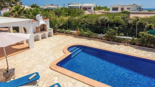 Une piscine avec des chaises longues, une table et un espace barbecue.