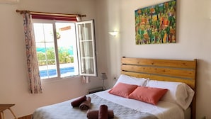 Une chambre à coucher avec un lit, une fenêtre avec des rideaux, un tableau au mur et une vue sur l’extérieur.