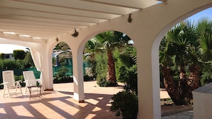 Un patio couvert doté de colonnes et d’arcs blancs, avec un sol carrelé et des plantes en pot.
