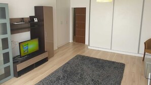 Moderni olohuone, jossa on litteänäyttöinen televisio, puulattia, harmaa matto, vaatekaappi ja riippuvalaisin.