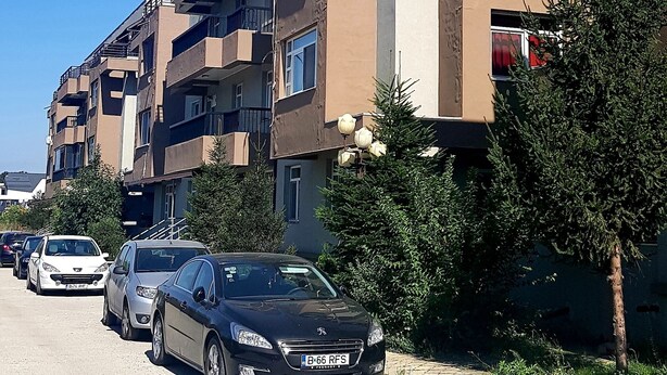 Rivi korkeita kerrostaloja, joissa on parvekkeita, parkkeerattuja autoja ja kirkas, sininen taivas.