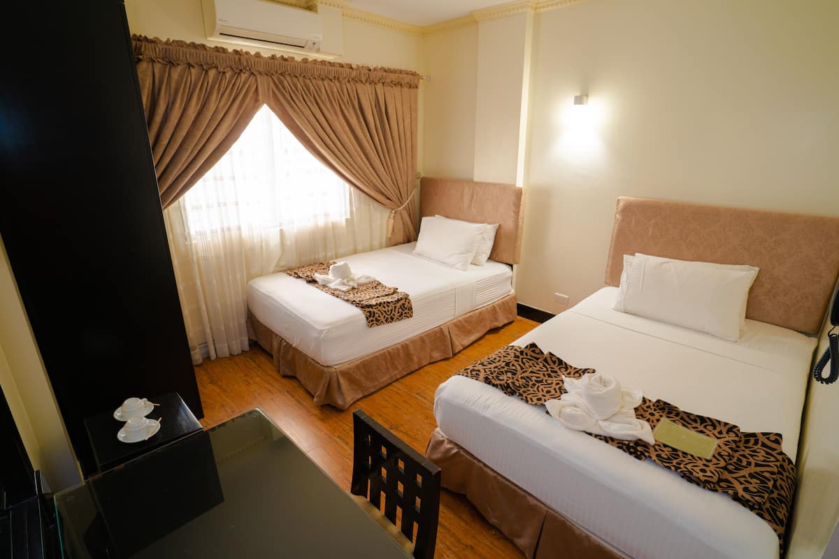 A hotel room with two beds, a desk, and a window with curtains.