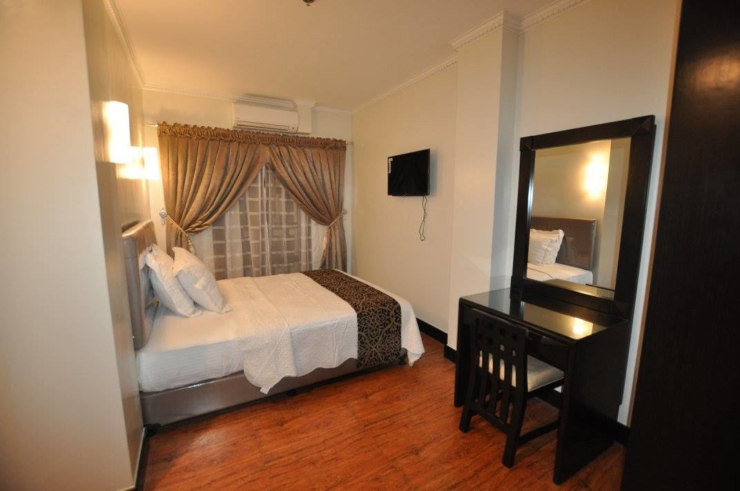 Een kleine hotelkamer met een enkel bed, een nachtkastje, een stoel, een bureau, een spiegel en een wandgemonteerde flatscreen-tv.