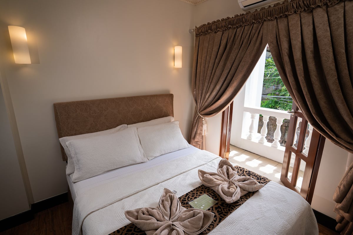 A neatly made bed with a headboard, two wall-mounted lights, and a window with curtains.