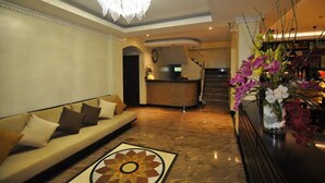A lobby with a reception desk, a sofa with cushions, a chandelier, and a vase with flowers.