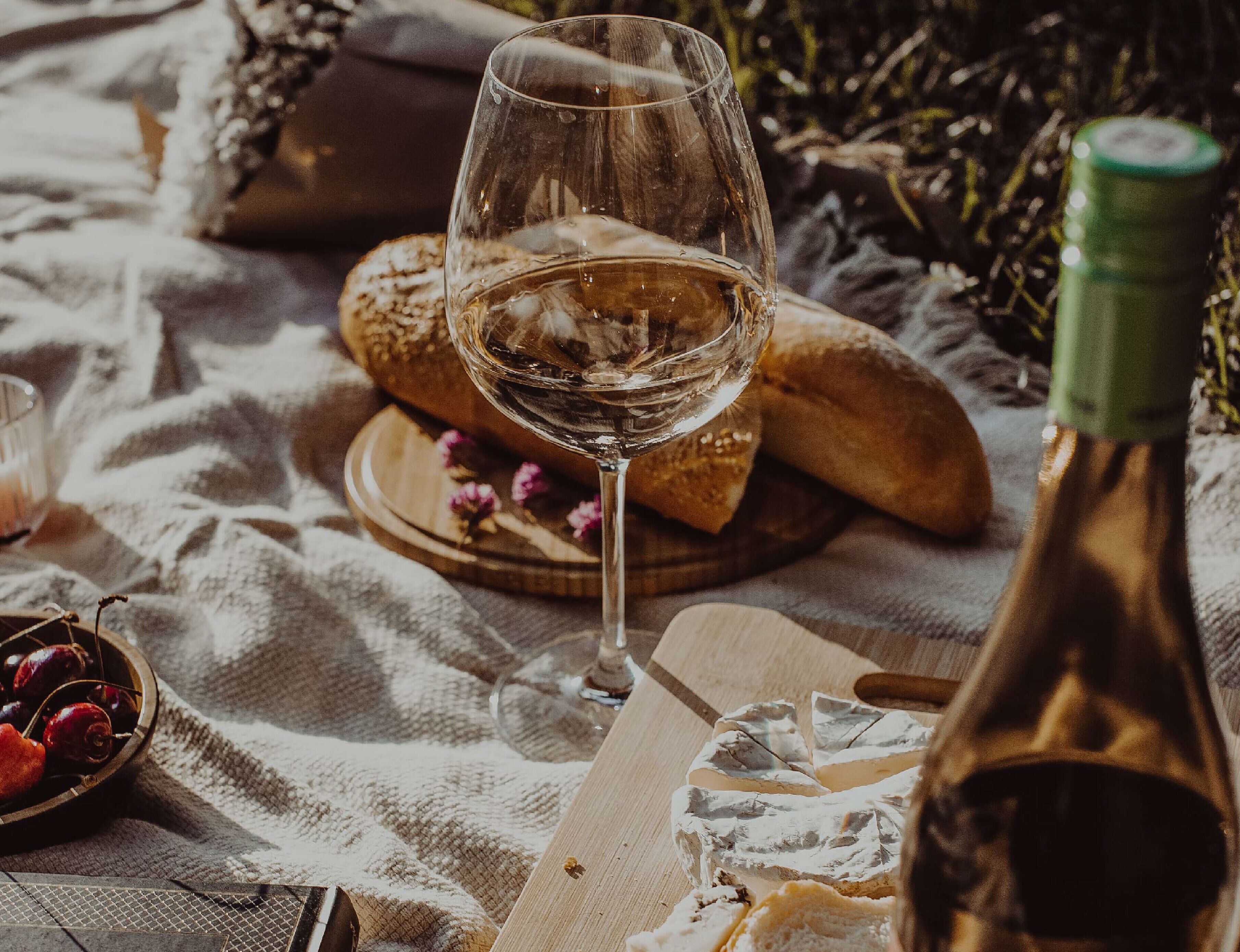 Un montaje para picnic con una copa de vino, pan, queso y una botella sobre una manta.