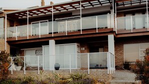 A two-story house with a balcony, a stone facade, and a garden with various plants.