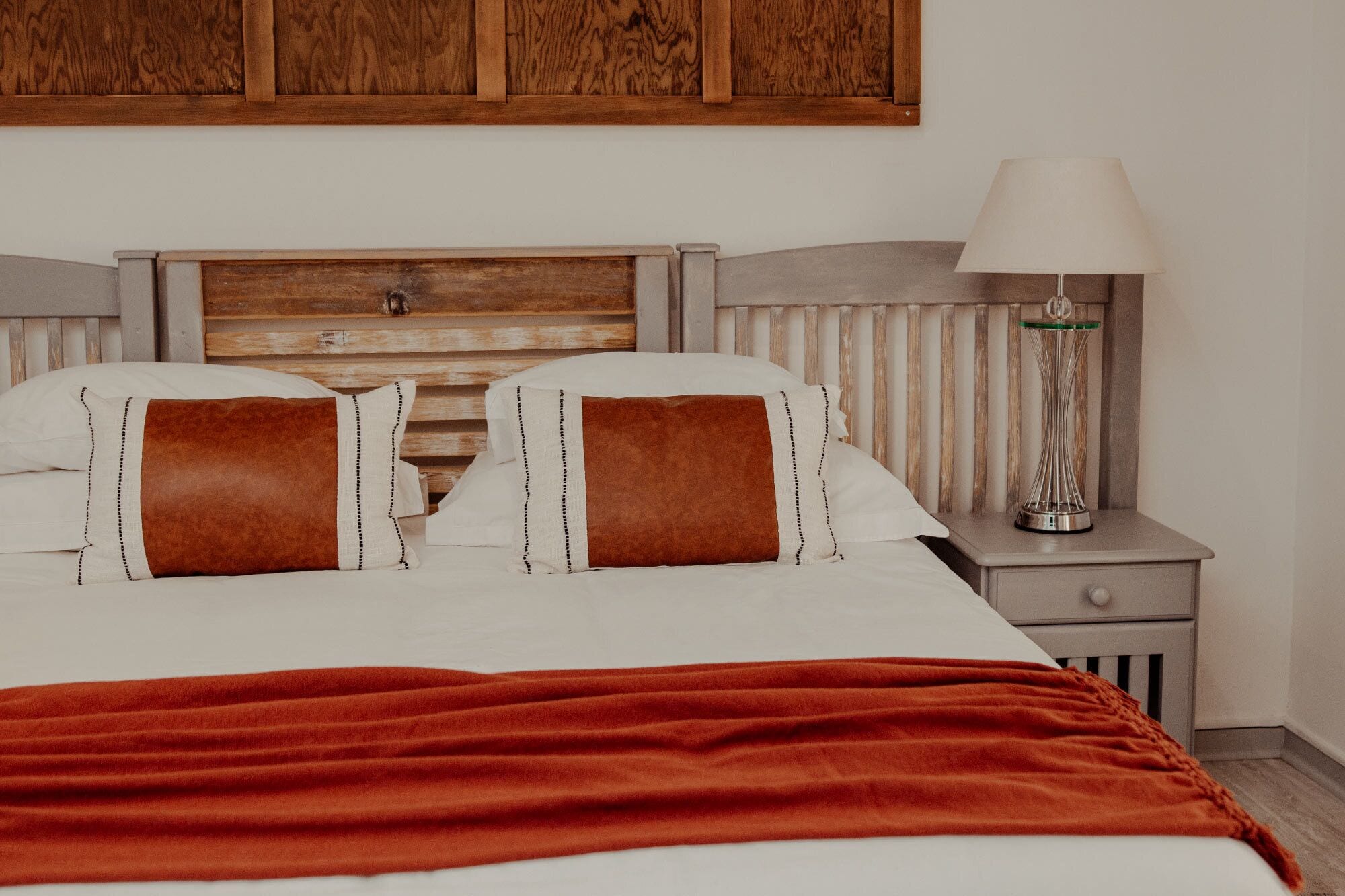 A neatly made bed with a red blanket, a wooden headboard, and a bedside lamp on a nightstand.