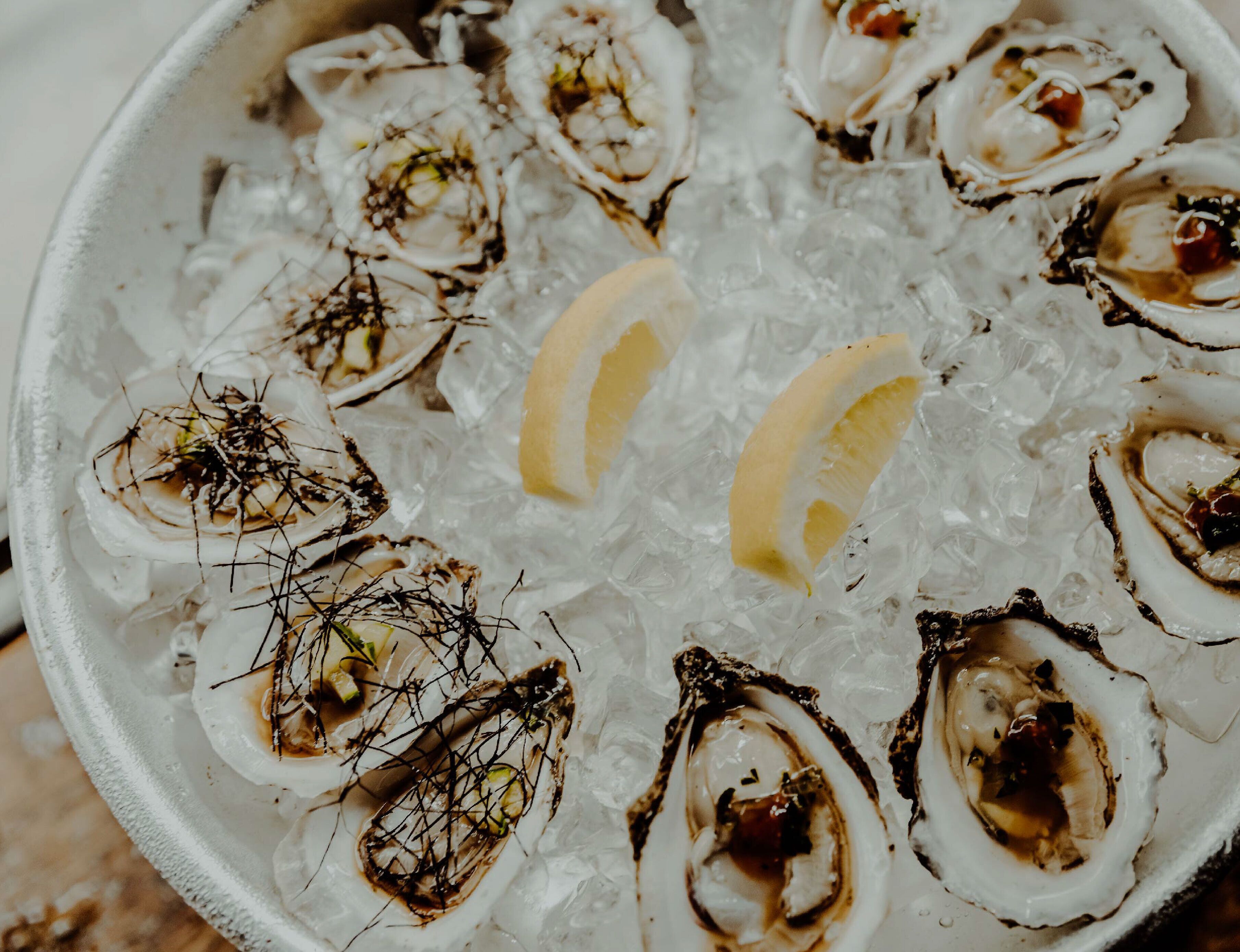 A bowl of oysters on ice with lemon wedges.