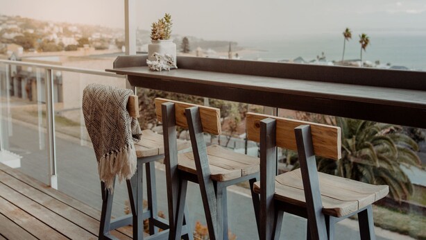 A balcony with wooden chairs and a table, overlooking a coastal view.