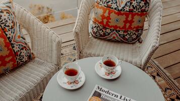 Two wicker chairs with patterned cushions, a round table with two teacups and saucers, and a magazine titled "Modern Living Home Decor".