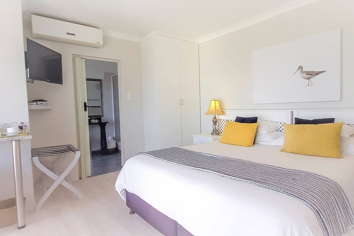 Habitación de hotel con cama, lámparas de noche, televisor y una mesita con tetera.