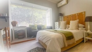 A bedroom with a bed, bedside tables, a dresser, a window with blinds, and a chair.