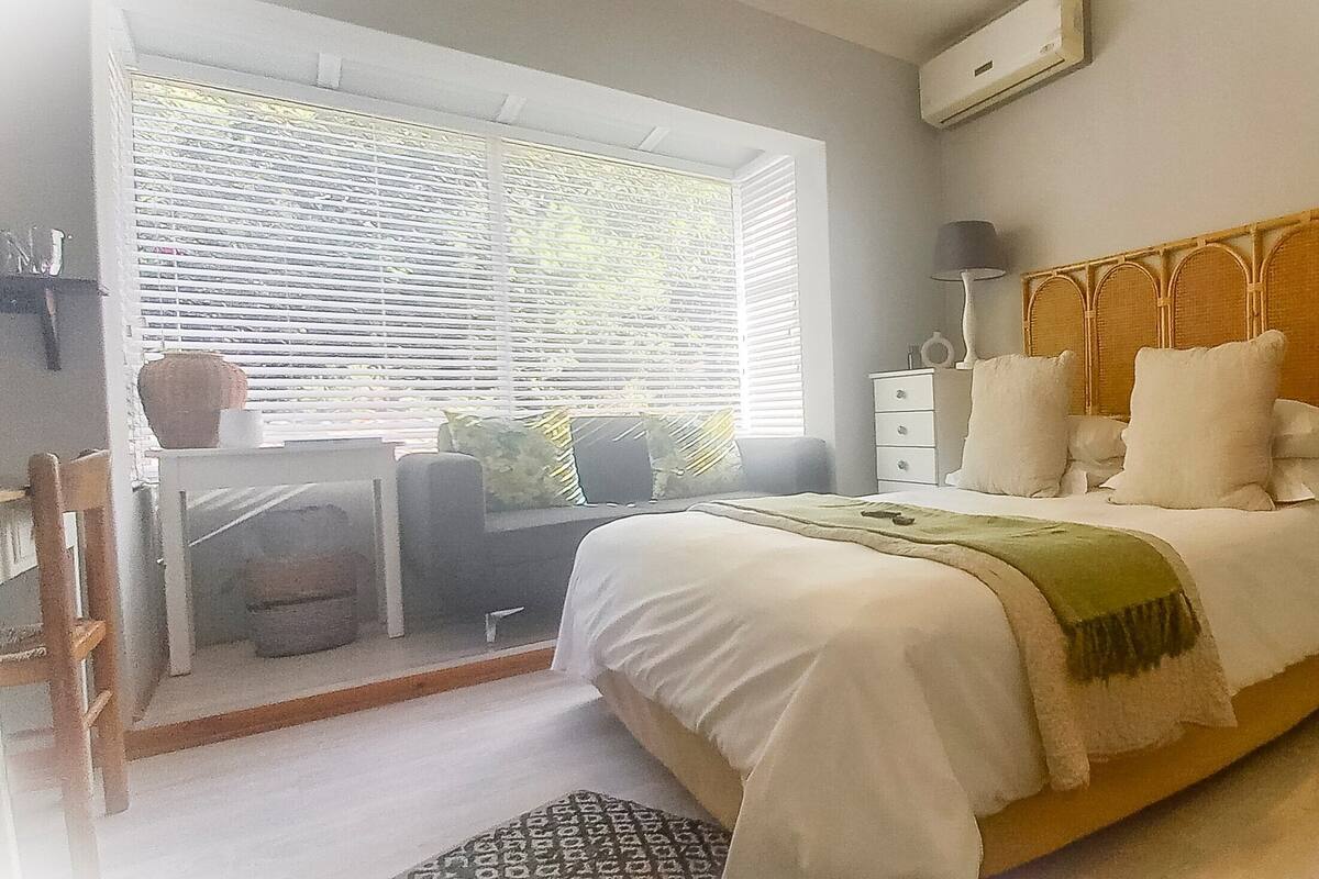 Un dormitorio con cama, mesitas de noche, cómoda, ventana con persianas y una silla.